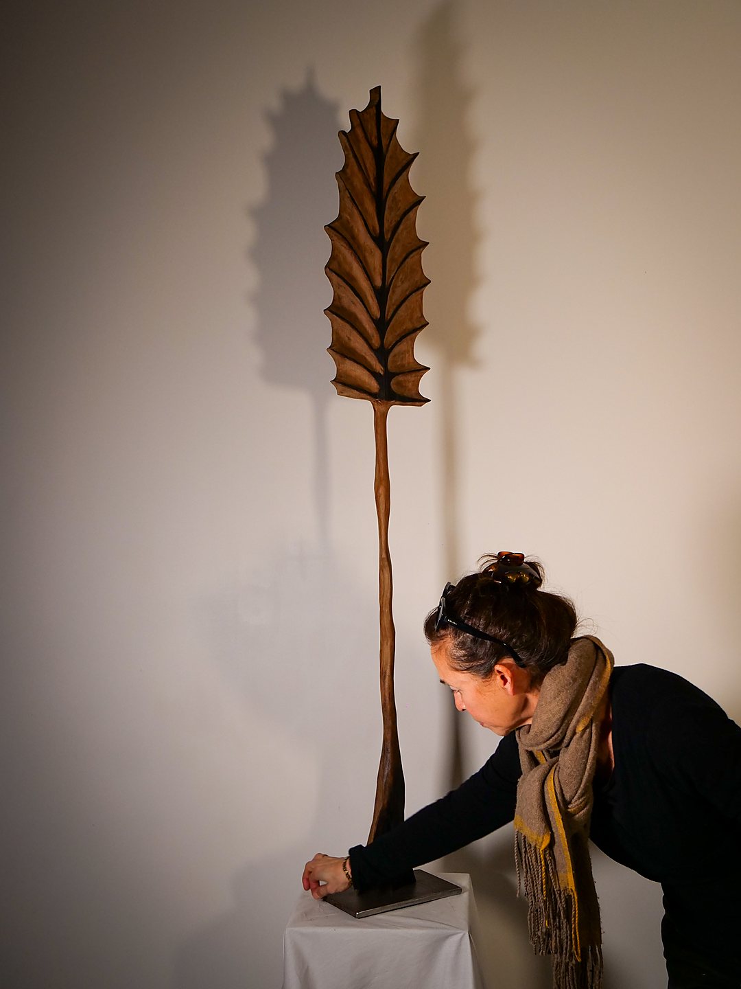 Florence Nguyen installant une grande feuille sculptée sur son socle, son ombre portée sur le mur de l'atelier